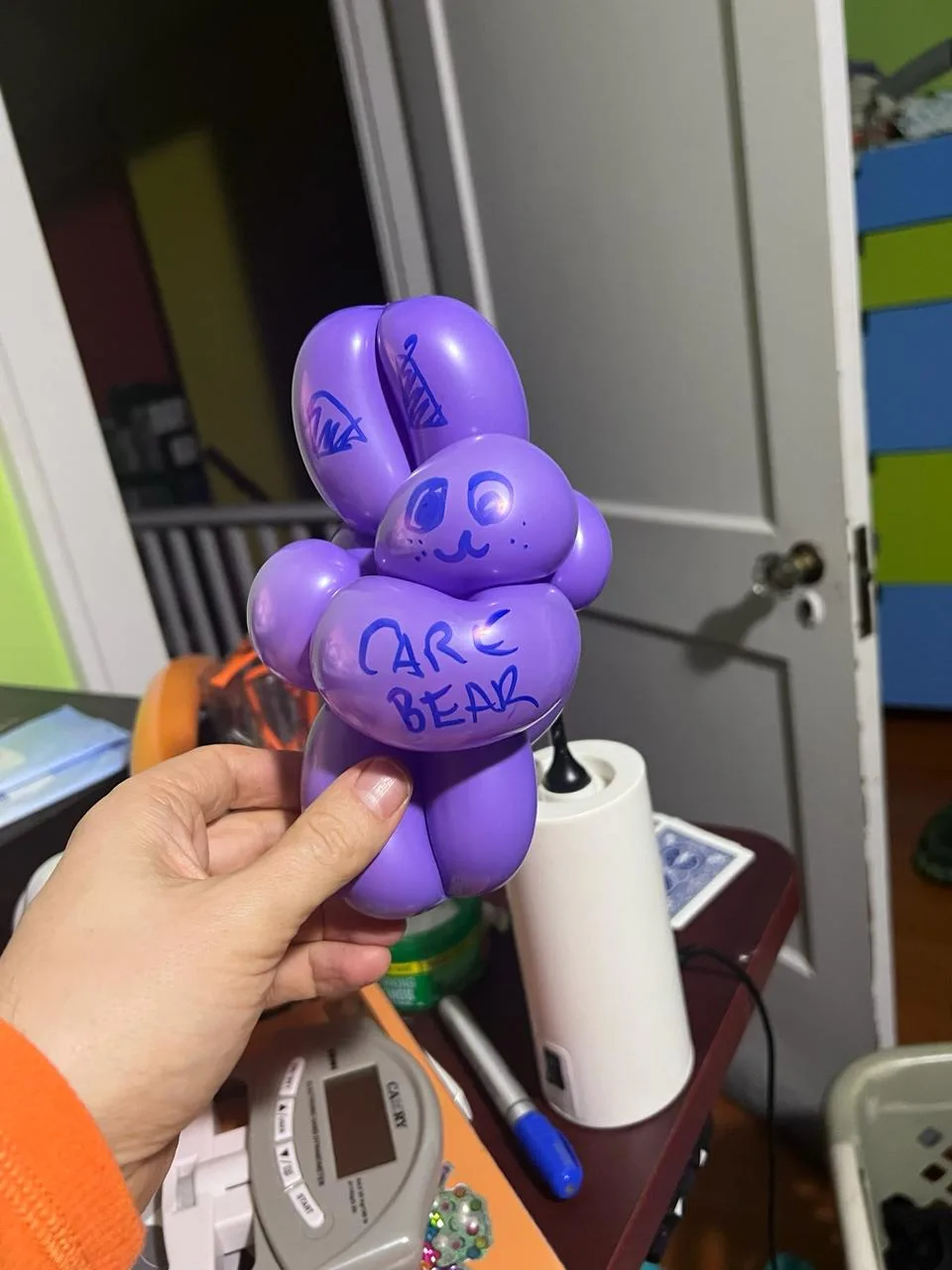 Small purple balloon bear with a marker-drawn face and CARE BEAR written on its belly, held in one hand