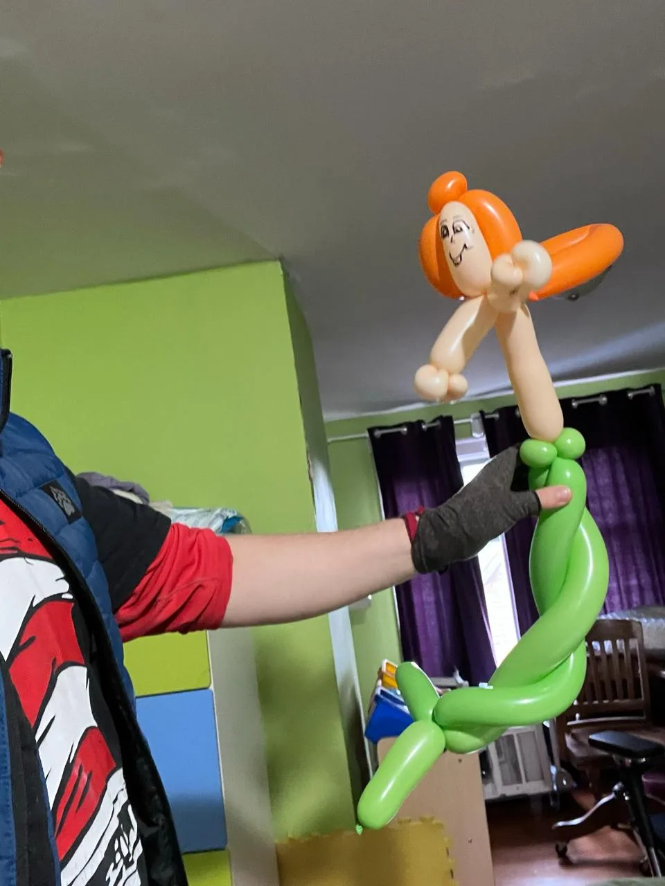Balloon mermaid with orange hair, peach arms and a curled green tail, held up at arm's length