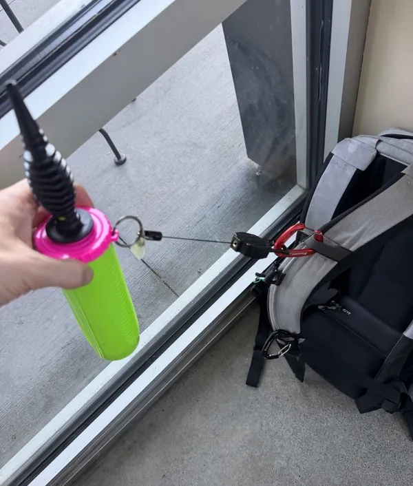 Green and pink hand balloon pump on a retractable reel, clipped with a red carabiner to a backpack shoulder strap
